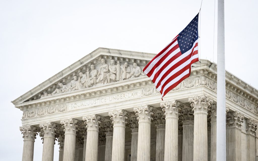 A picture of the supreme court, with the US flag waving in front of the phrase 